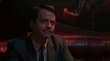 Movie still from “Auto Focus” (2002), directed by Paul Schrader – A man in a suit and tie sitting in a chair; Close Up shot, Over the shoulder angle