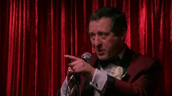 A man in a red jacket is speaking into a microphone