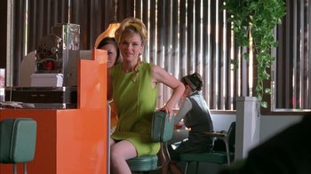 Movie still from “Auto Focus” (2002), directed by Paul Schrader – A woman sitting on top of a green chair; Medium shot, Low angle