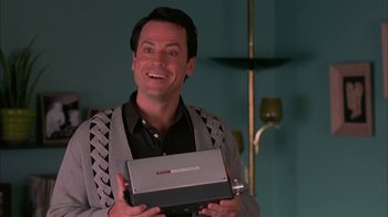 Movie still from “Auto Focus” (2002), directed by Paul Schrader – A smiling man holding an electronic device in his hands; Close Up shot, Low angle