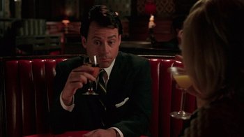 Movie still from “Auto Focus” (2002), directed by Paul Schrader – A man sitting at a table holding a wine glass; Medium shot, Over the shoulder angle