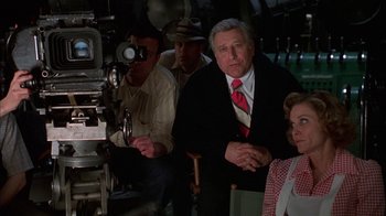 Movie still from “Auto Focus” (2002), directed by Paul Schrader – A group of people standing around a camera; Medium shot, Over the shoulder angle