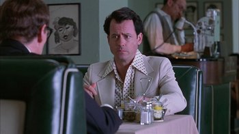 Movie still from “Auto Focus” (2002), directed by Paul Schrader – A man sitting at a table in front of a plate of food; Medium shot, Over the shoulder angle