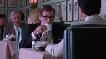 Movie still from “Auto Focus” (2002), directed by Paul Schrader – A man sitting at a table drinking a cup of coffee; Medium shot, Over the shoulder angle