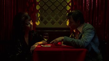 Movie still from “Auto Focus” (2002), directed by Paul Schrader – A man and a woman sitting at a table with a glass of wine in front of them; Medium shot, High angle