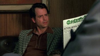 Movie still from “Auto Focus” (2002), directed by Paul Schrader – A man sitting in a chair reading a newspaper; Close Up shot, Over the shoulder angle