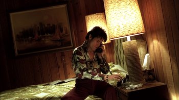 Movie still from “Auto Focus” (2002), directed by Paul Schrader – A man sitting on a bed talking on a phone; Medium shot, Low angle