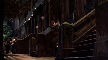 Movie still from “Avalon” (1990), directed by Barry Levinson – Two people sitting on steps in front of a building at night; Extreme Wide shot, High angle