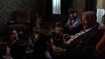 Movie still from “Avalon” (1990), directed by Barry Levinson – A group of people sitting in a living room with a dog; Medium shot, Over the shoulder angle