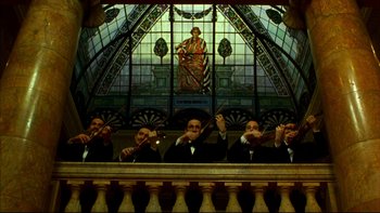 Movie still from “Avalon” (1990), directed by Barry Levinson – A group of men in black suits playing musical instruments in front of a stained glass window; Extreme Wide shot, Low angle