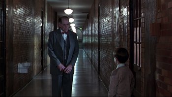 Movie still from “Avalon” (1990), directed by Barry Levinson – A man in a suit and tie standing next to a boy in a hallway; Wide shot, Over the shoulder angle