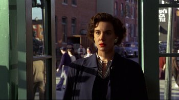 Movie still from “Avalon” (1990), directed by Barry Levinson – A woman standing in front of a window with people in the background; Medium shot, Low angle
