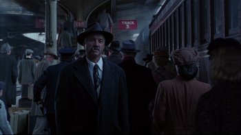 Movie still from “Avalon” (1990), directed by Barry Levinson – A man wearing a suit and hat standing in front of a group of people; Medium shot, Low angle