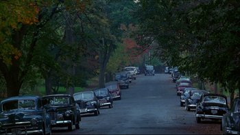 Movie still from “Avalon” (1990), directed by Barry Levinson – A street filled with lots of parked cars next to trees; Extreme Wide shot, High angle