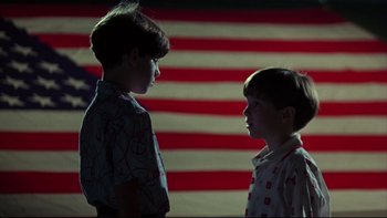 Movie still from “Avalon” (1990), directed by Barry Levinson – Two young boys standing next to each other in front of an american flag; Medium shot, Low angle