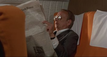 Movie still from “Avanti!” (1972), directed by Billy Wilder – An older man wearing glasses reading a newspaper; Medium shot, Over the shoulder angle