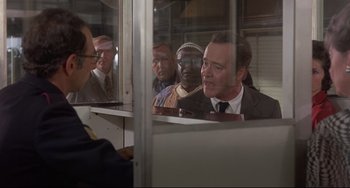 Movie still from “Avanti!” (1972), directed by Billy Wilder – A group of people sitting in front of a glass window; Medium shot, Over the shoulder angle