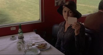 Movie still from “Avanti!” (1972), directed by Billy Wilder – A woman sitting at a table holding up a card; Medium shot, Over the shoulder angle