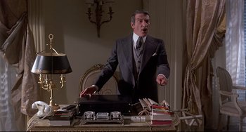 Movie still from “Avanti!” (1972), directed by Billy Wilder – A man standing at a desk with a briefcase; Medium shot, Low angle