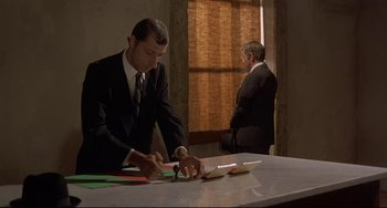 Movie still from “Avanti!” (1972), directed by Billy Wilder – A man in a black suit cutting paper with a pair of scissors; Wide shot, High angle