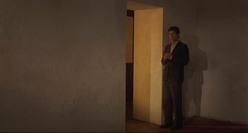 Movie still from “Avanti!” (1972), directed by Billy Wilder – A man in a suit standing next to an open door; Wide shot, Low angle