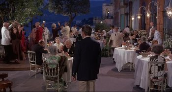 Movie still from “Avanti!” (1972), directed by Billy Wilder – A group of people sitting at tables with food on it; Wide shot, High angle
