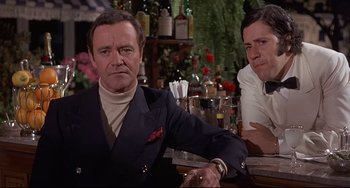 Movie still from “Avanti!” (1972), directed by Billy Wilder – A man sitting at a bar next to another man; Medium shot, Low angle