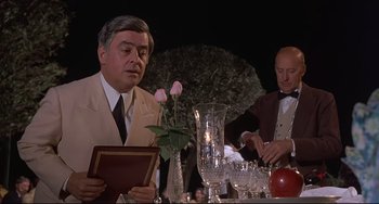 Movie still from “Avanti!” (1972), directed by Billy Wilder – A man sitting at a table in front of a glass vase; Medium shot, Over the shoulder angle