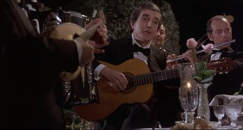 Movie still from “Avanti!” (1972), directed by Billy Wilder – A group of people sitting around a table with a guitar; Medium shot, Low angle