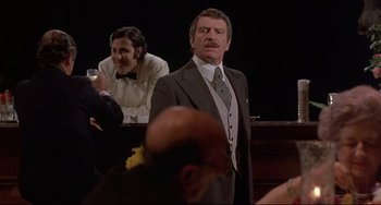 Movie still from “Avanti!” (1972), directed by Billy Wilder – A man standing in front of a crowd of people; Medium shot, Over the shoulder angle