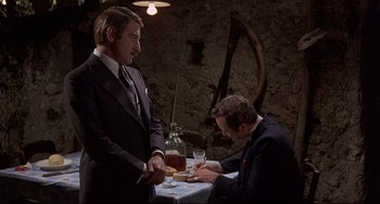 Movie still from “Avanti!” (1972), directed by Billy Wilder – A man in a suit and tie sitting at a dinner table; Medium shot, Over the shoulder angle