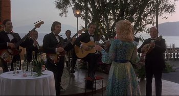 Movie still from “Avanti!” (1972), directed by Billy Wilder – A group of people standing on a patio playing instruments; Wide shot, Low angle
