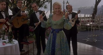 Movie still from “Avanti!” (1972), directed by Billy Wilder – A woman in a dress holding a bunch of musical instruments; Medium shot, Low angle