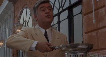 Movie still from “Avanti!” (1972), directed by Billy Wilder – A man in a suit and tie holding a frying pan; Medium shot, Low angle
