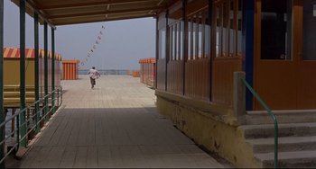 Movie still from “Avanti!” (1972), directed by Billy Wilder – A man riding a skate board down a wooden pier; Extreme Wide shot, High angle