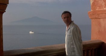 Movie still from “Avanti!” (1972), directed by Billy Wilder – A man standing next to a body of water with mountains in the background; Medium shot, Low angle