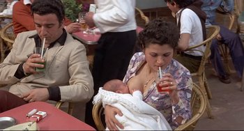 Movie still from “Avanti!” (1972), directed by Billy Wilder – A woman holding a baby while drinking a beverage; Medium shot, High angle
