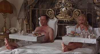 Movie still from “Avanti!” (1972), directed by Billy Wilder – A man sitting on top of a bed next to a woman; Medium shot, High angle