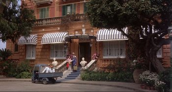 Movie still from “Avanti!” (1972), directed by Billy Wilder – A man driving a truck down a street past a building; Wide shot, Low angle