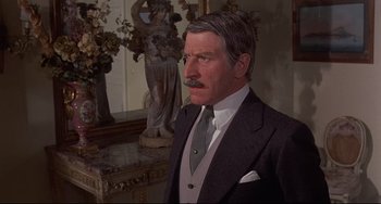 Movie still from “Avanti!” (1972), directed by Billy Wilder – An older man wearing a suit and tie in front of a statue; Medium shot, Over the shoulder angle