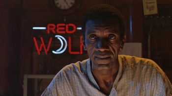 A man in a checkered shirt is in front of a red wolf sign