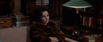 Movie still from “BUtterfield 8” (1960), directed by Daniel Mann – A woman sitting in a chair wearing a fur coat; Close Up shot, High angle