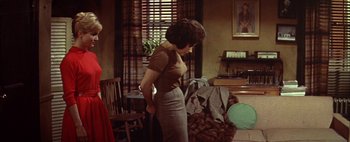 A woman standing in a living room with her hands behind her back