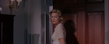 Movie still from “BUtterfield 8” (1960), directed by Daniel Mann – A woman in a white dress standing in front of a door; Medium shot, Over the shoulder angle