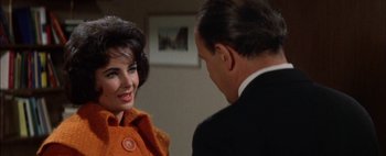 Movie still from “BUtterfield 8” (1960), directed by Daniel Mann – A woman in an orange coat talking to a man in a black suit; Close Up shot, Over the shoulder angle