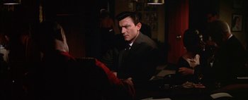 Movie still from “BUtterfield 8” (1960), directed by Daniel Mann – A man sitting at a table in a dark room; Medium shot, Over the shoulder angle