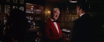 Movie still from “BUtterfield 8” (1960), directed by Daniel Mann – An older man in a red jacket is holding a wine glass; Medium shot, Over the shoulder angle