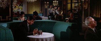 Movie still from “BUtterfield 8” (1960), directed by Daniel Mann – A man sitting at a table in front of a glass of wine; Wide shot, High angle