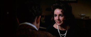 Movie still from “BUtterfield 8” (1960), directed by Daniel Mann – A woman wearing a black dress and pearls talking to a man wearing a suit; Close Up shot, Over the shoulder angle
