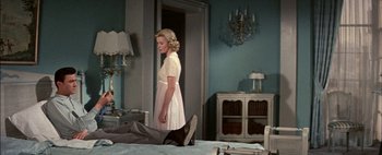 Movie still from “BUtterfield 8” (1960), directed by Daniel Mann – A woman standing in front of a man laying on a bed; Wide shot, High angle